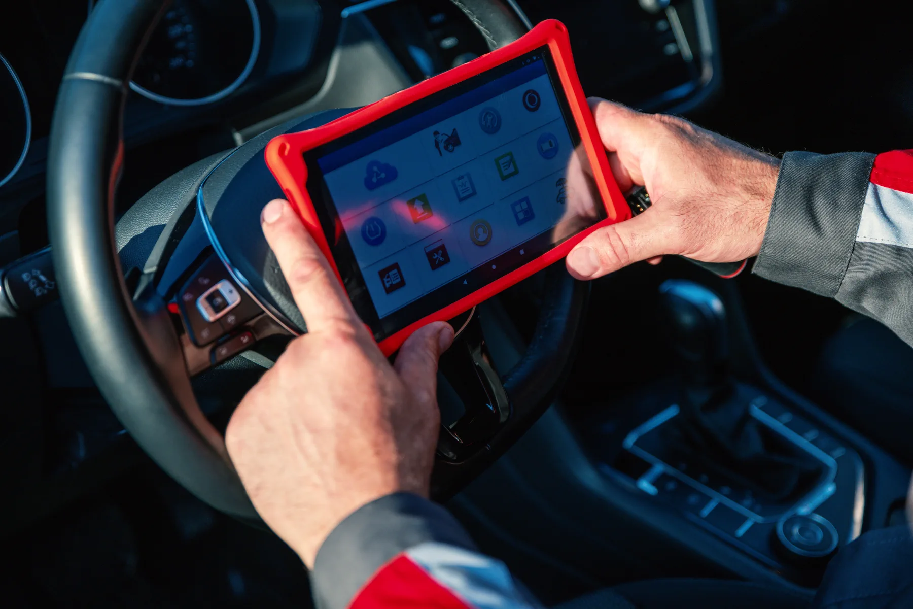 Technician using a red diagnostic tablet inside a vehicle
